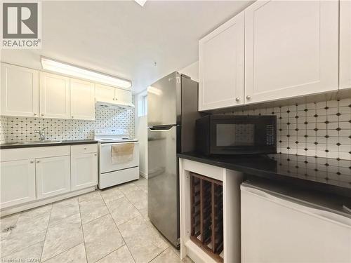 Kitchen with white cabinetry, black countertops, patterned tile backsplash, stainless steel refrigerator, and tile flooring - 380 Grangewood Drive, Waterloo, ON 