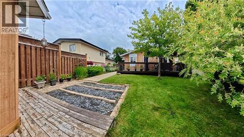Expansive backyard featuring a manicured lawn, a full-width wood deck, and raised garden beds - 380 Grangewood Drive, Waterloo, ON 