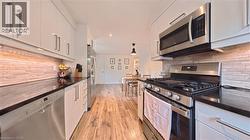 Kitchen featuring white high-gloss cabinetry, stainless steel appliances, dark countertops, and a textured tile backsplash - 