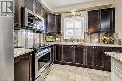 Kitchen featuring dark wood cabinetry, light granite countertops, a stainless steel range, and an over-range microwave - 