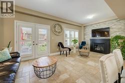 Spacious living area featuring large format tile flooring, a stone accent wall with an integrated fireplace and mantel, and white French doors leading to exterior space - 
