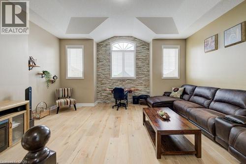 Living area featuring light wood-finish flooring, a tray ceiling, and a stone accent wall with an arched window - 300 Watervale Crescent, Kitchener, ON 