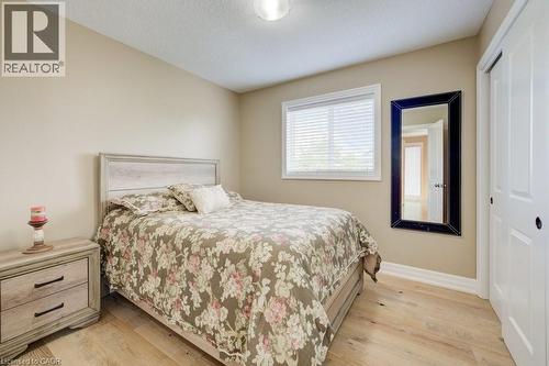 Bedroom featuring wood-finish flooring, neutral wall tones, a window with blinds, and white bi-fold closet doors - 300 Watervale Crescent, Kitchener, ON 