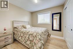 Bedroom featuring wood-finish flooring, neutral wall tones, a window with blinds, and white bi-fold closet doors - 