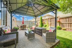 Expansive patio featuring a permanent gazebo structure, string lighting, exposed aggregate concrete, and a manicured lawn - 