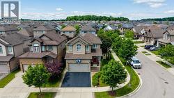 Two-story residence featuring a neutral-toned exterior, an attached garage with a paved driveway, and mature landscaping - 