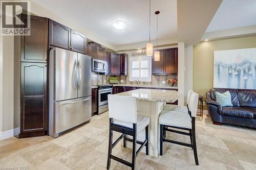 Kitchen featuring dark wood cabinetry, stainless steel appliances, a tile backsplash, and a light-toned countertop island with pendant lighting - 300 Watervale Crescent, Kitchener, ON 