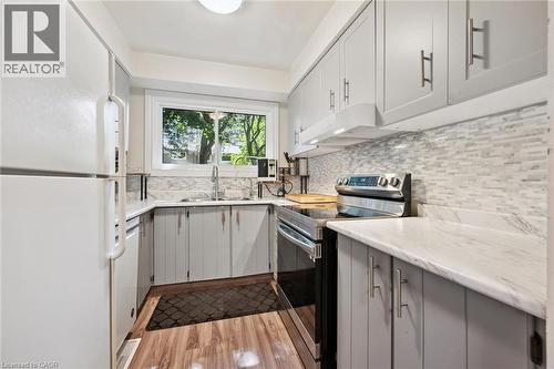 Modern kitchen featuring light gray cabinetry, white countertops, tile backsplash, and wood-finish flooring - 46 Cedarwoods Crescent Unit# 53, Kitchener, ON - Indoor Photo Showing Kitchen With Double Sink