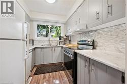 Modern kitchen featuring light gray cabinetry, white countertops, tile backsplash, and wood-finish flooring - 