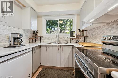 U-shaped kitchen with white cabinetry, light-toned countertops, tile backsplash, and a stainless steel sink - 46 Cedarwoods Crescent Unit# 53, Kitchener, ON - Indoor Photo Showing Kitchen With Double Sink