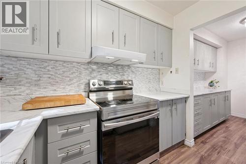 Recessed lighting, wood-finish flooring, light grey cabinetry with brushed nickel hardware, light-toned countertop, and a tile backsplash - 46 Cedarwoods Crescent Unit# 53, Kitchener, ON - Indoor Photo Showing Kitchen With Upgraded Kitchen