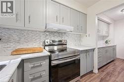 Recessed lighting, wood-finish flooring, light grey cabinetry with brushed nickel hardware, light-toned countertop, and a tile backsplash - 