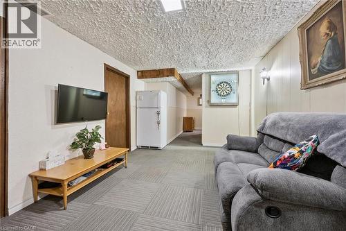 Wall-mounted television with a light wood-finish console, patterned carpet tile flooring, and overhead recessed lighting - 46 Cedarwoods Crescent Unit# 53, Kitchener, ON - Indoor