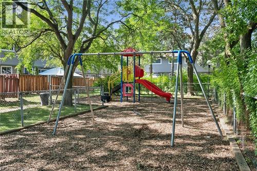 Playground area featuring a swing set, multi-level play structure with slide, wood chip ground cover, and chain-link fencing - 46 Cedarwoods Crescent Unit# 53, Kitchener, ON - Outdoor