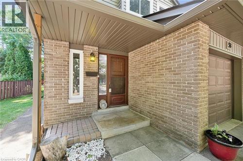 Brick exterior featuring a covered entry, wood-paneled garage door, and decorative sidelight - 46 Cedarwoods Crescent Unit# 53, Kitchener, ON - Outdoor With Exterior