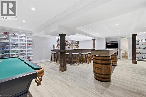 Recessed lighting illuminates the wood-finish flooring, custom bar with seating, built-in shelving, and exposed structural columns - 2312 Ridgeview Court, Burlington, ON - Indoor Photo Showing Other Room
