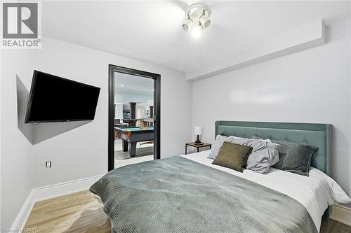 Wood-finish flooring with white baseboards, a ceiling-mounted light fixture, and a built-in wall-mounted television - 2312 Ridgeview Court, Burlington, ON - Indoor Photo Showing Bedroom