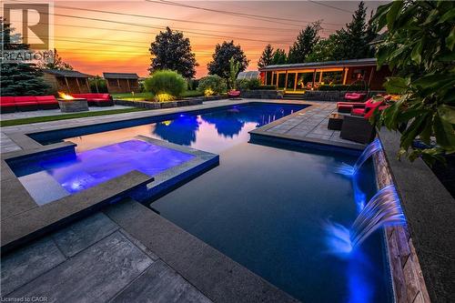 Expansive outdoor living area featuring a multi-level pool with integrated spa, waterfall features, stone hardscaping, and a fire pit - 2312 Ridgeview Court, Burlington, ON - Outdoor With In Ground Pool With Deck Patio Veranda