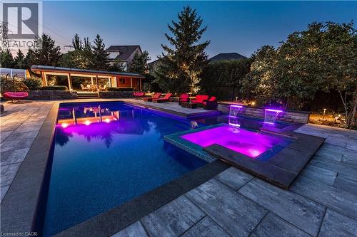 Outdoor leisure area featuring a rectangular swimming pool, integrated spa, adjacent covered patio, and stone paver hardscaping - 2312 Ridgeview Court, Burlington, ON - Outdoor With In Ground Pool With Deck Patio Veranda