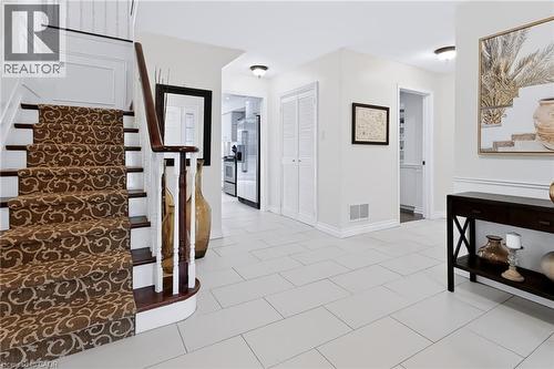 Gracious entryway featuring a curved staircase with a patterned runner, crisp white wainscoting, and large format tile flooring - 4248 Dunvegan Road, Burlington, ON 