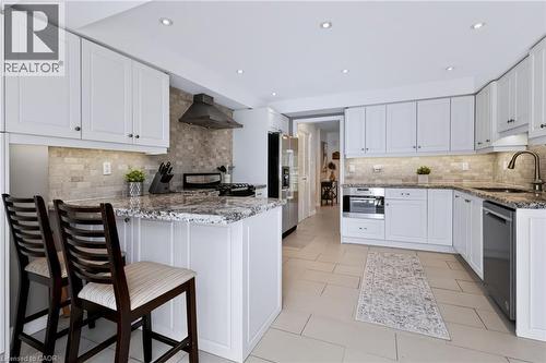 Contemporary kitchen featuring white cabinetry, stone countertops, a tile backsplash, stainless steel appliances, and recessed lighting - 4248 Dunvegan Road, Burlington, ON 