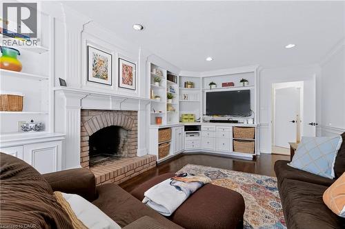 Wood-finish flooring with a brick fireplace, white mantel, and built-in shelving - 4248 Dunvegan Road, Burlington, ON 