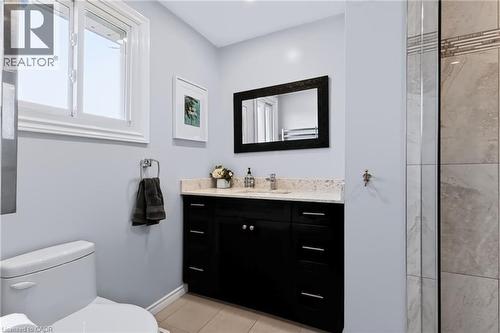 Single-handle chrome faucet, dark wood vanity with undermount sink, light-colored countertop, tiled flooring, and a large window - 4248 Dunvegan Road, Burlington, ON 