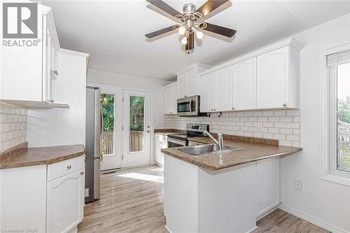White cabinetry with brushed nickel hardware, light-toned wood-finish flooring, white subway tile backsplash, stainless steel appliances, and double glass-paneled doors - 47 Queensway Drive, Strathroy, ON - Indoor Photo Showing Kitchen