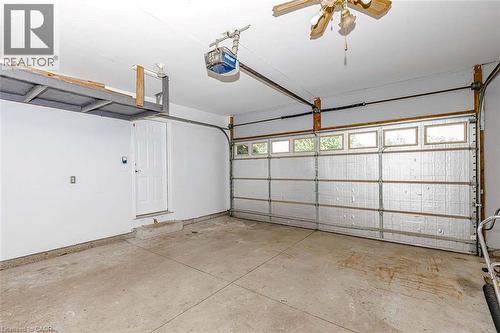 Attached garage with concrete flooring, overhead storage, side entry door, and garage door with upper window panels - 47 Queensway Drive, Strathroy, ON - Indoor Photo Showing Garage