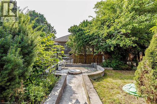 Landscaped backyard featuring mature trees, a concrete patio, and a built-in fire pit with stone surround - 47 Queensway Drive, Strathroy, ON - Outdoor