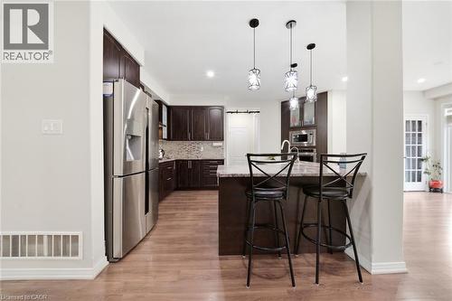 Kitchen featuring wood-finish flooring, dark wood cabinetry, stainless steel appliances, a tile backsplash, and a central island with pendant lighting - 57 Cheevers Road, Brantford, ON - Indoor Photo Showing Kitchen With Upgraded Kitchen