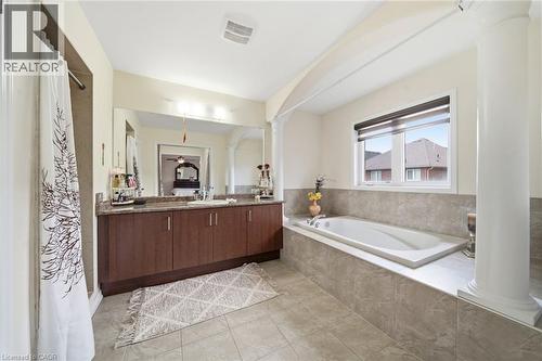 Built-in soaking tub with tiled surround, double vanity with stone-finish countertop, and integrated mirror - 57 Cheevers Road, Brantford, ON - Indoor Photo Showing Bathroom