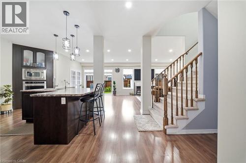 Open concept living space featuring wood-finish flooring, a kitchen island with stone countertop, built-in stainless steel appliances, pendant lighting, and a carpeted staircase with wood banister - 57 Cheevers Road, Brantford, ON - Indoor Photo Showing Kitchen With Upgraded Kitchen
