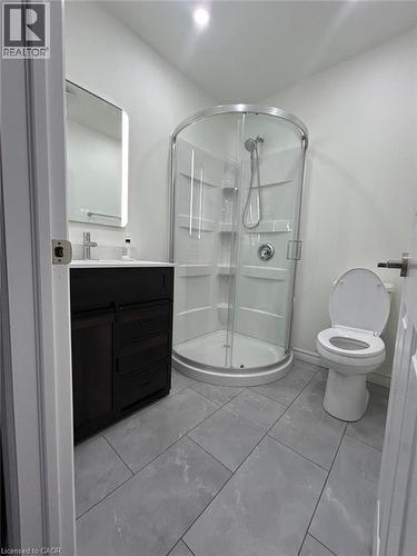 Gray tile flooring, dark wood-finish vanity with countertop, illuminated mirror, and a curved glass shower enclosure - 31 Sofitel Drive, Kitchener, ON - Indoor Photo Showing Bathroom