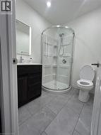 Gray tile flooring, dark wood-finish vanity with countertop, illuminated mirror, and a curved glass shower enclosure - 