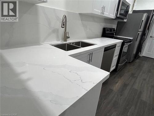 White countertops with integrated sink, white upper and lower cabinetry, stainless steel appliances, and wood-finish flooring - 31 Sofitel Drive, Kitchener, ON - Indoor Photo Showing Kitchen With Double Sink
