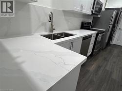 White countertops with integrated sink, white upper and lower cabinetry, stainless steel appliances, and wood-finish flooring - 
