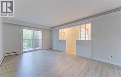 Spacious room featuring wood-finish flooring, light-colored walls, and a sliding glass door leading to a balcony with metal railings - 