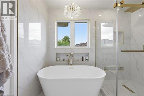 Freestanding soaking tub with a wall-mounted faucet, complemented by a walk-in shower featuring a glass enclosure and built-in shelving - 738 Fourth Line, Milton, ON - Indoor Photo Showing Bathroom