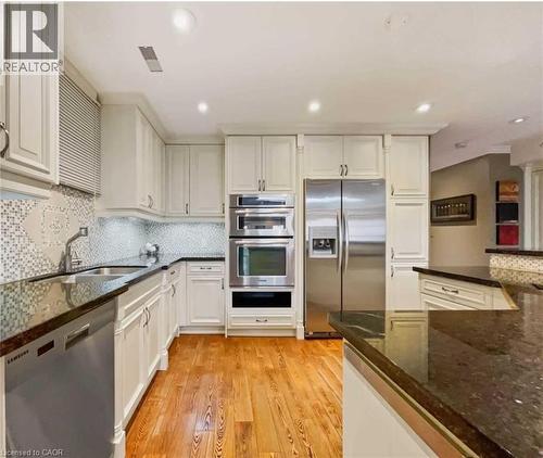 Wood-finish flooring, white cabinetry, stainless steel appliances, dark stone countertops, and a mosaic tile backsplash - 453 Brant Street, Burlington, ON 