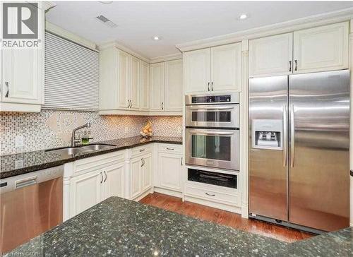 White shaker-style cabinetry with crown molding, stainless steel appliances, dark stone countertops, mosaic tile backsplash, and wood-finish flooring - 453 Brant Street, Burlington, ON 