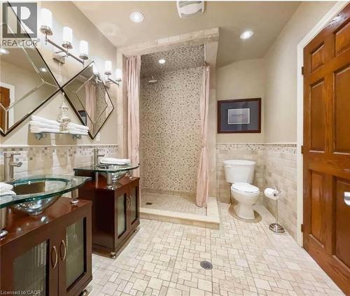Dual glass vessel sinks with wood-finish vanities, a mosaic tile shower, and patterned floor tiles - 453 Brant Street, Burlington, ON 