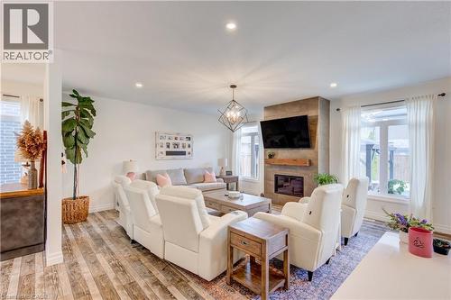 Living room featuring wood-finish flooring, a contemporary chandelier, recessed lighting, a fireplace with a wood mantel, and large windows - 1061 Eagletrace Drive Unit# 174, London, ON - Indoor Photo Showing Living Room With Fireplace