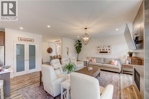 Recessed lighting, wood-finish flooring, geometric ceiling light fixture, fireplace with tiled surround, and frosted glass French doors - 1061 Eagletrace Drive Unit# 174, London, ON - Indoor Photo Showing Living Room