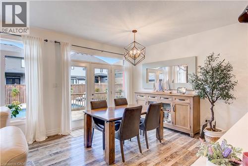 Wood-finish flooring with a geometric chandelier, white walls, and a light wood-tone buffet - 1061 Eagletrace Drive Unit# 174, London, ON - Indoor Photo Showing Dining Room