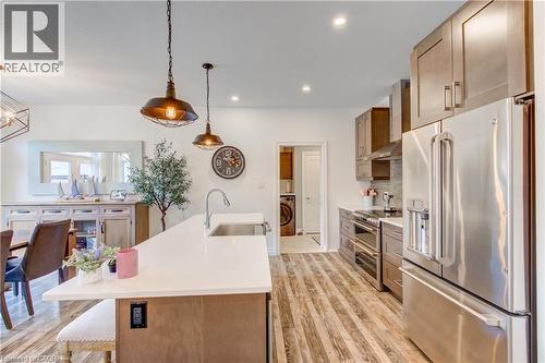 Open-concept kitchen featuring wood-finish flooring, a central island with a white countertop and integrated sink, stainless steel appliances, and pendant lighting - 1061 Eagletrace Drive Unit# 174, London, ON - Indoor Photo Showing Kitchen With Upgraded Kitchen