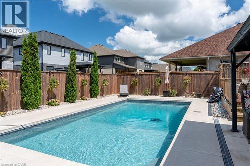 In-ground swimming pool with surrounding concrete decking, complemented by a wood fence and mature trees - 1061 Eagletrace Drive Unit# 174, London, ON - Outdoor With In Ground Pool With Deck Patio Veranda
