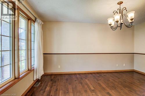 Wood-finish flooring, accent wall with chair rail molding, multi-pane windows, and a classic chandelier - 3 Cora Drive, Kitchener, ON - Indoor Photo Showing Other Room