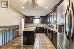 Kitchen featuring dark wood cabinetry, light-toned countertops, stainless steel appliances, and tile flooring - 