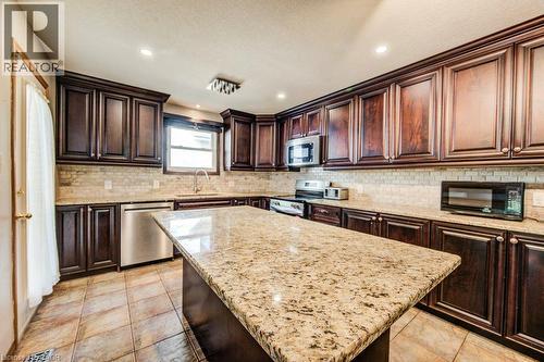 Kitchen featuring dark wood cabinetry, light-toned granite countertops, tile backsplash, and stainless steel appliances - 3 Cora Drive, Kitchener, ON - Indoor Photo Showing Kitchen With Upgraded Kitchen